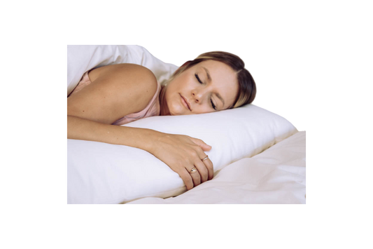 A person peacefully sleeping on the Shepherd's Dream Wool Filled Body Pillow with an organic cotton cover, nestled under a white blanket. Their face is relaxed and they are lying on their side, with a hand resting softly on the wool-filled pillow.