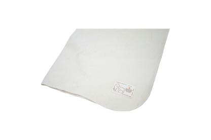 The Washable Wool Crib Mattress Protector by Shepherd's Dream, made from natural wool in a soft off-white hue, includes a small tag with a simple line drawing of an animal and text. Displayed against a black background, it serves as an elegant addition to any baby bedding collection.