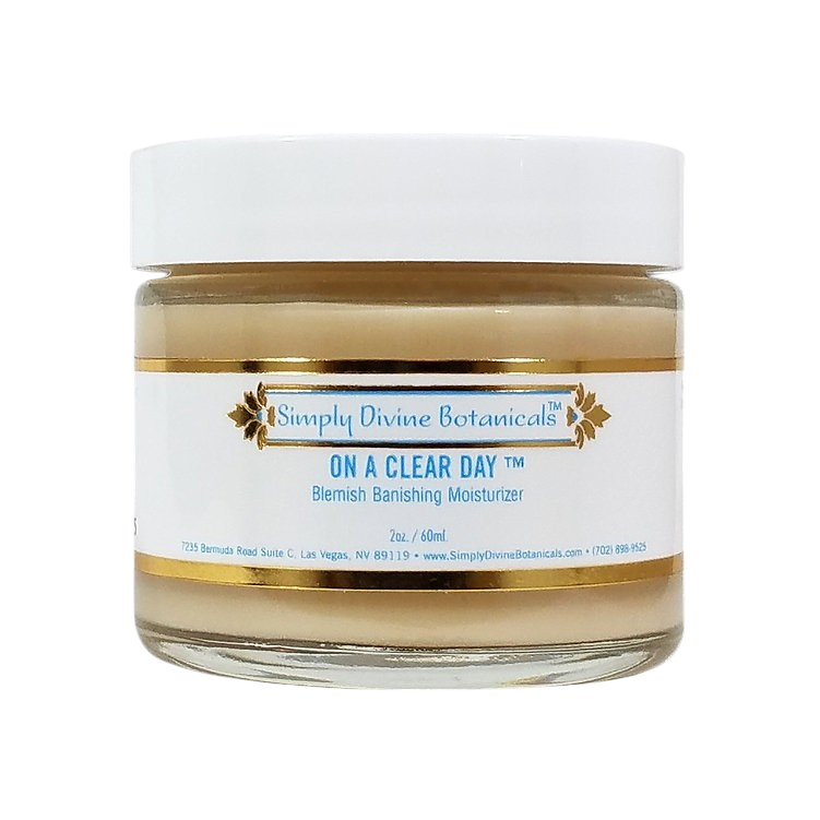 A jar of Simply Divine Botanicals On A Clear Day Blemish Banishing Moisturizer with vegan ingredients, a white lid, and a gold-accented label featuring blue text on a white background.