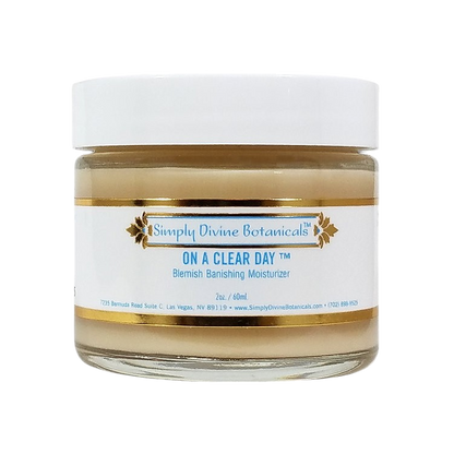 A jar of Simply Divine Botanicals On A Clear Day Blemish Banishing Moisturizer with vegan ingredients, a white lid, and a gold-accented label featuring blue text on a white background.