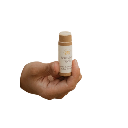 A hand holds a small, cylindrical cardboard tube labeled "Honeybee Hippie" and "Vanilla & Chamomile," set against a white background.