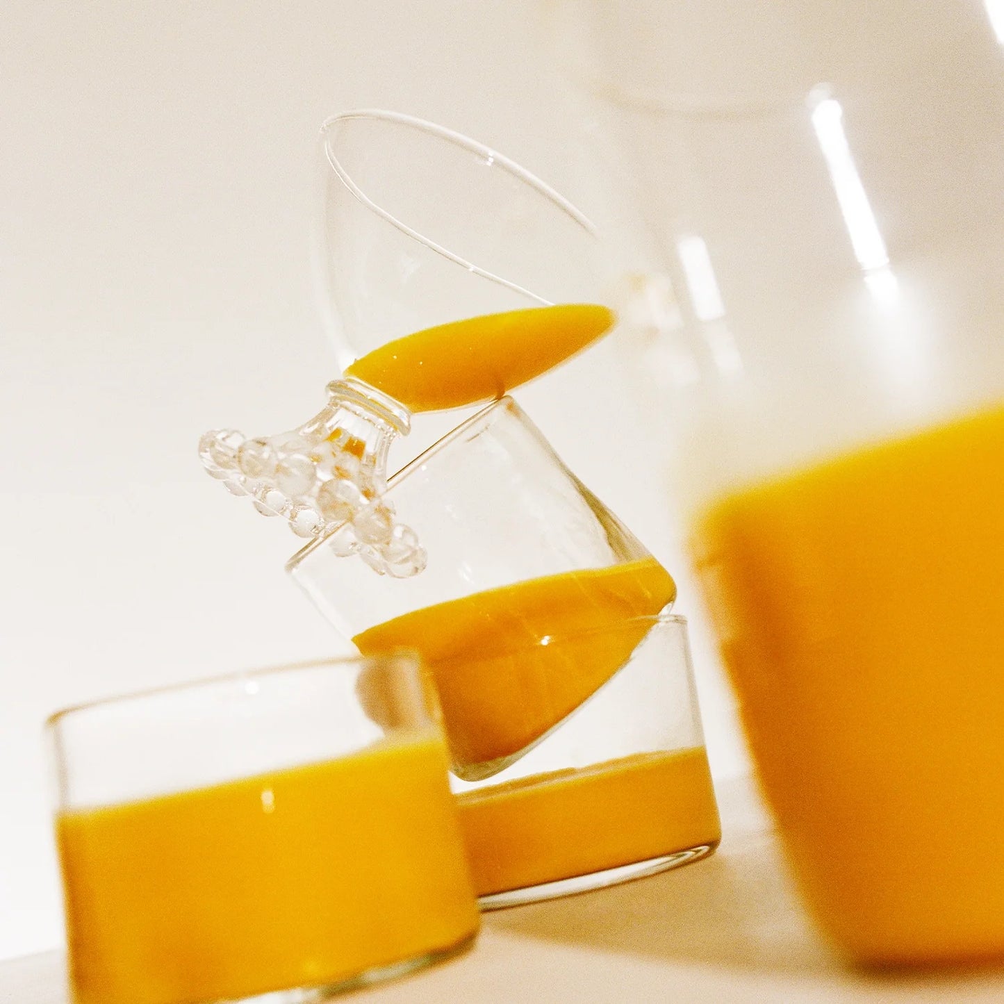 A tilted image displays three glasses from THE FULLEST's Warm Feelings 30-Day Supply, each filled with a saffron latte whose thick, yellow-orange hue exudes warmth. The creatively stacked glasses form a playful and dynamic composition against a plain white backdrop, hinting at mood enhancement with every sip.