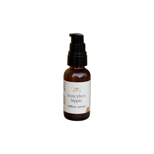 A small brown bottle with a black pump, labeled "Honeybee Hippie Saffron Serum," a hydrating botanical elixir for skin brightening, stands upright on a plain white background.