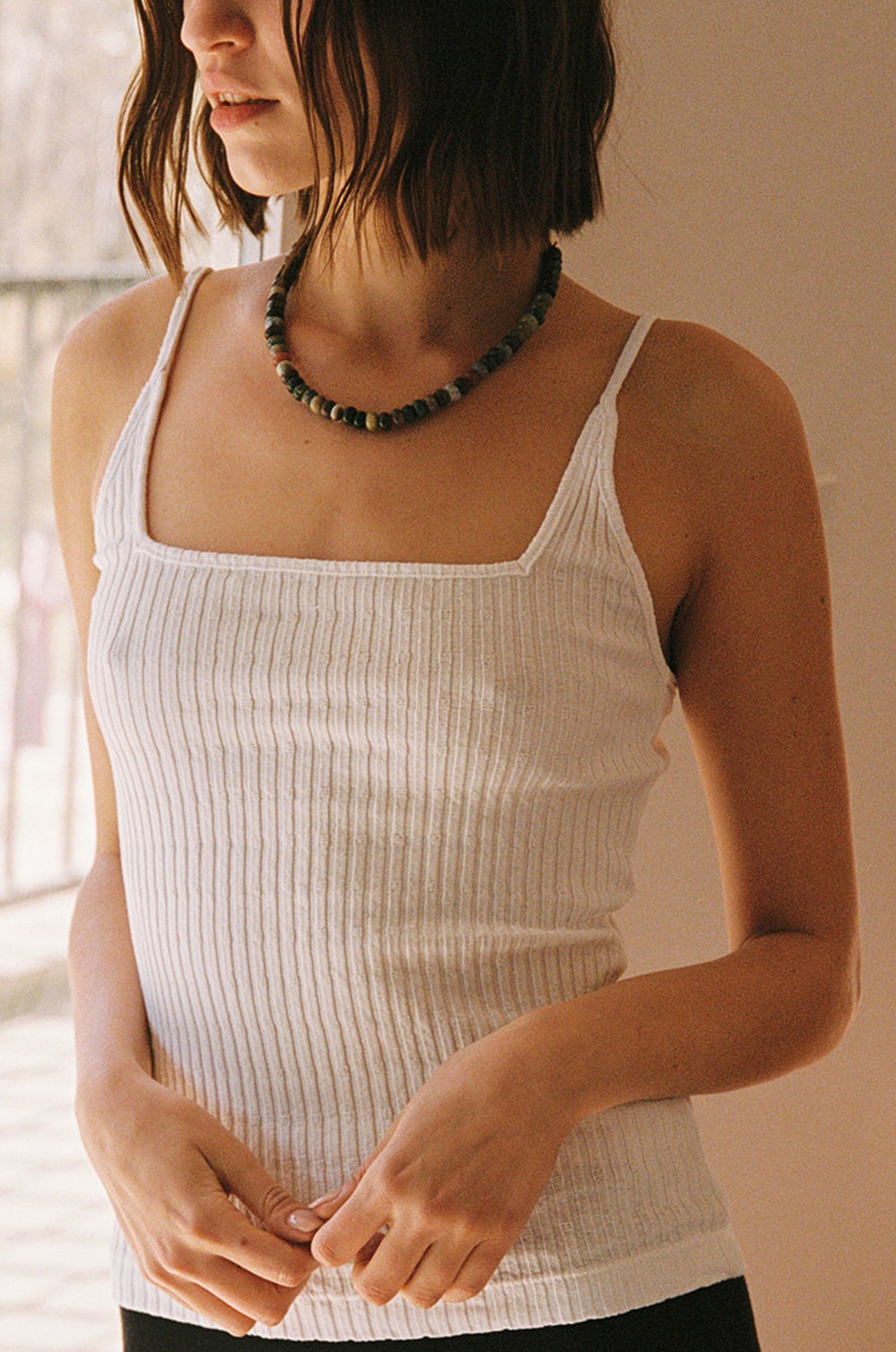 White A woman with shoulder-length brown hair wears the LA Relaxed Pointelle Square Cami and a beaded necklace, standing indoors in soft light. Her face is partially out of the frame.