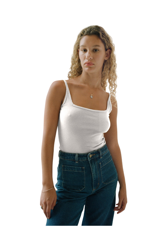 A young woman with curly blonde hair, dressed in a 90's style Organic Square Cami by LA Relaxed and high-waisted jeans, stands against a plain background.