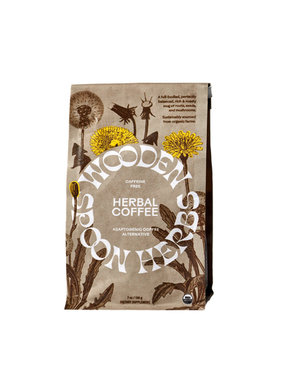 A brown and cream-colored packaging of WOODEN SPOON HERBS Herbal Coffee is shown, adorned with botanical illustrations that include dandelions. The text emphasizes that this caffeine-free blend contains adaptogenic mushrooms and serves as a coffee alternative. The net weight is 7 oz (198 g).
