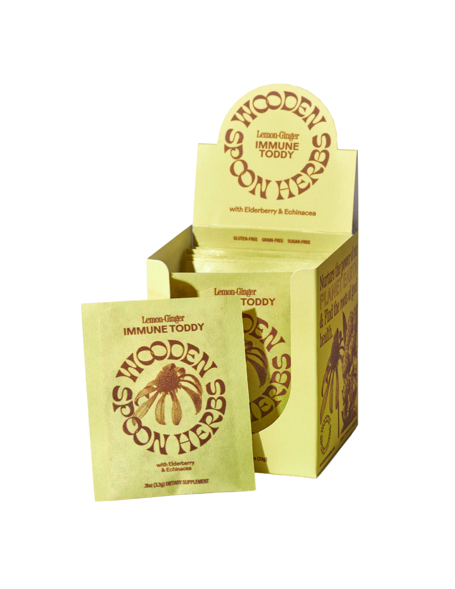 A yellow box of WOODEN SPOON HERBS Lemon-Ginger Immune Toddy Sachets, designed for immune support with elderberry and echinacea, is displayed. One sachet is positioned in front of the open box, showcasing the front label and the brown logo featuring a wooden spoon with herbs.