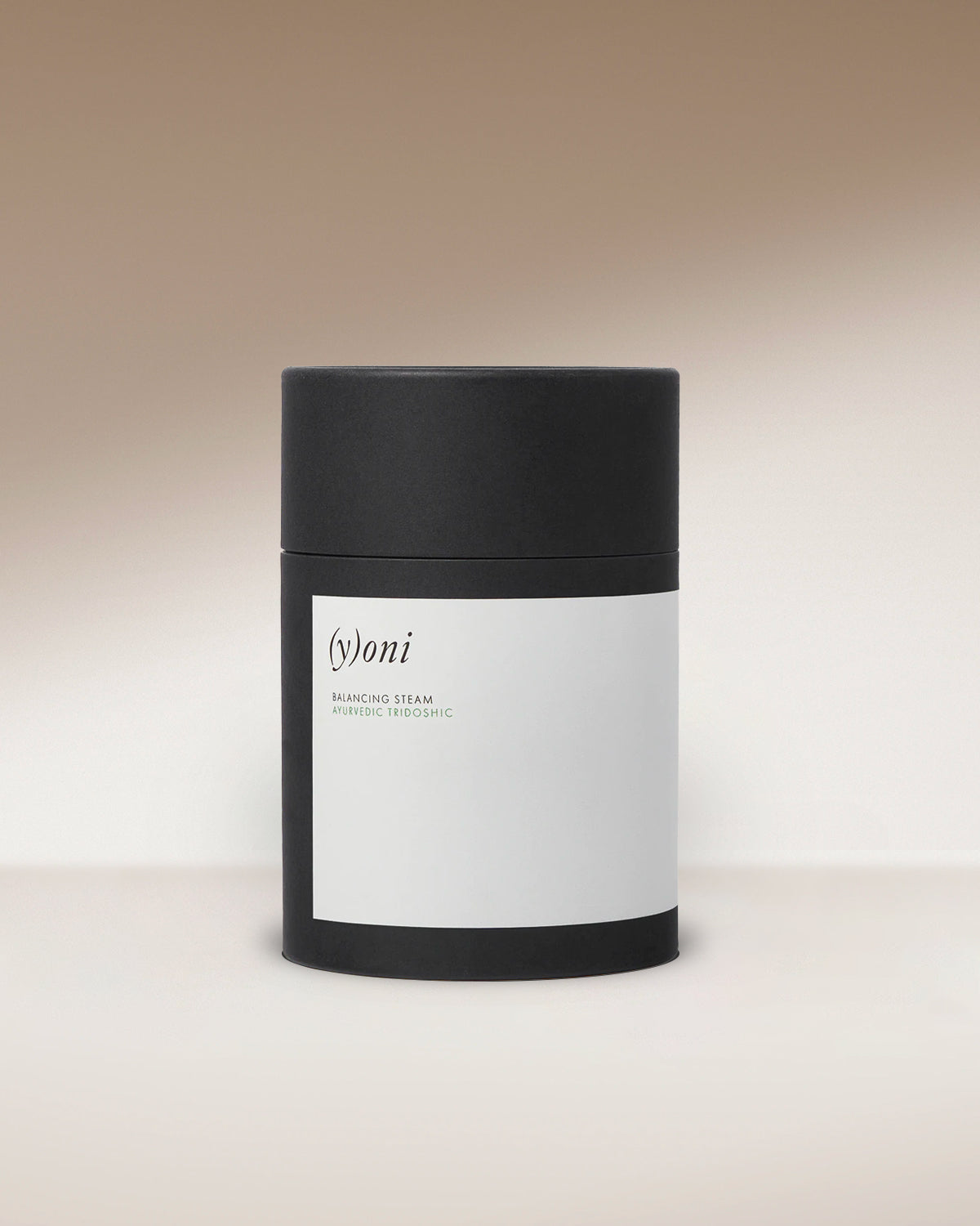 A cylindrical product with a black lid and base, featuring a white label in the middle. The label bears the text "(y)oni Fertility Steam" and "Surya," touted for its blend of Ayurvedic herbs. The background is a gradient of light to dark beige.